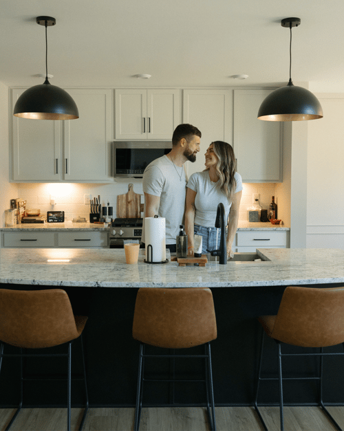 Couple standing together in a bright, modern kitchen in their new home, designed by a new home builder, featuring an open-concept layout, spacious island, and contemporary finishes