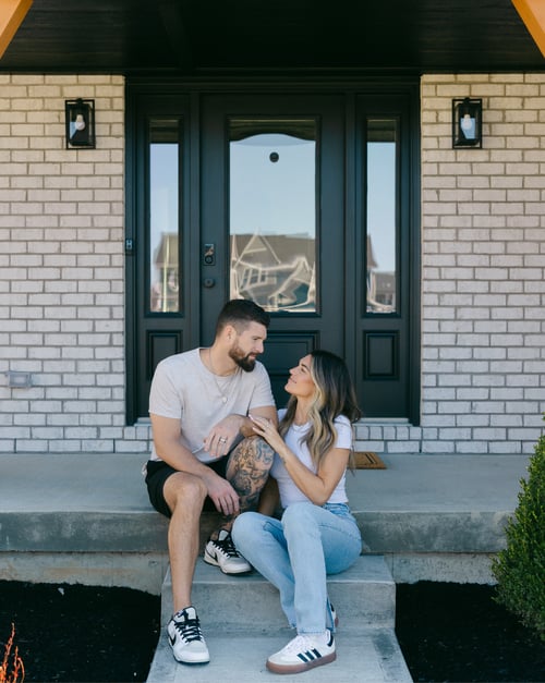 Couple standing outside their new home, smiling together in front of a beautifully designed exterior by a new home builder, featuring strong curb appeal and a welcoming entryway.