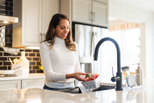 Woman standing at the kitchen sink in a modern Fischer Homes kitchen, surrounded by bright lighting, clean countertops, and contemporary finishes.